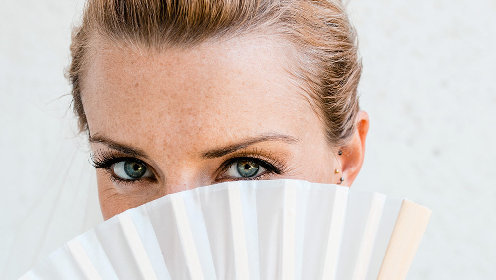 bride at destination wedding, hiding face behind fan