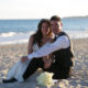 bride and groom sit together on sandy beach