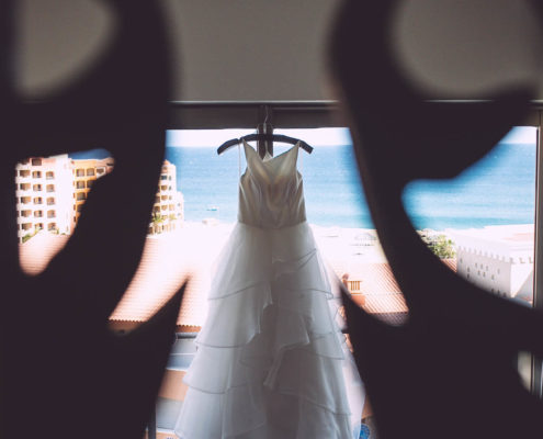 wedding dress hanging up with beach and ocean behind it.