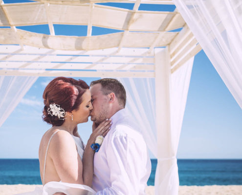 bride and groom kiss under beach wedding canopy