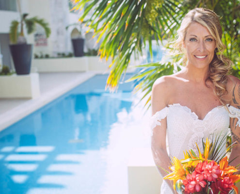 smiling bride poses with bouquet by pool