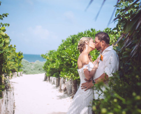 newly married couple kiss along sandy pathway