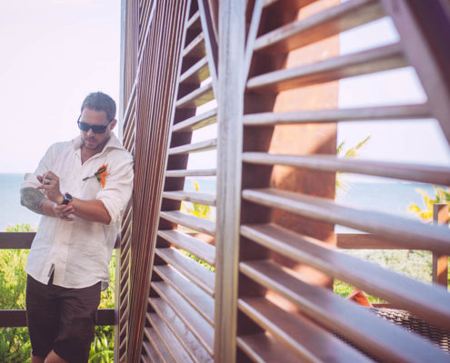 groom waits alone by window with wooden blinds