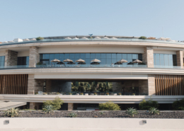 Exterior view of Dreams Bahia Mita resort in Mexico, featuring modern stone architecture, expansive glass windows, rooftop umbrellas, and open terraces overlooking the property.
