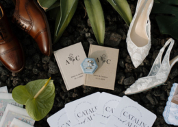 Wedding details arranged on dark volcanic rocks, featuring brown leather shoes, white bridal heels, personalized stationery, ceremony fans, and tropical greenery for a Dreams Bahia Mita wedding.