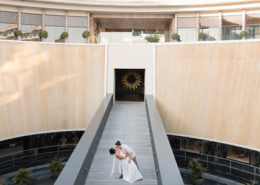Two brides sharing a romantic kiss on a long modern walkway surrounded by curved stone walls and water features during their Dreams Bahia Mita wedding in Mexico.