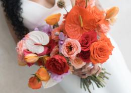 Bride in a white wedding dress holding a vibrant tropical bouquet of orange anthuriums, coral roses, pink orchids, and peach flowers for her Puerto Vallarta wedding in Mexico.