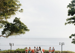 Wide view of a romantic Puerto Vallarta wedding ceremony overlooking the Pacific Ocean, with seated guests, white chairs, tropical trees, and colorful floral arrangements.