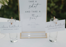 Personalized sweetheart table seating display featuring a framed "Take a Shot and Take a Seat" sign with two small glasses and name cards for a Mexico destination wedding.