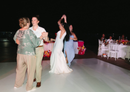 Bride in a beige suit dancing with an older guest while her partner in a white wedding dress celebrates nearby during their lively Dreams Bahia Mita wedding reception.