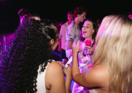 Bride with long curly hair celebrating with wedding guests beneath colorful purple party lights, capturing a joyful moment during her Mexico destination wedding reception.