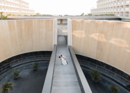 Overhead view of a bride in a flowing white wedding dress posing on a modern walkway between curved stone walls and water features at Dreams Bahia Mita resort in Mexico.