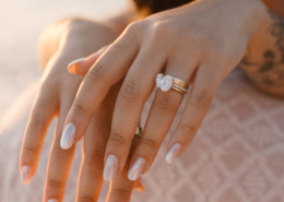 Close-up of a bride's hand resting on her partner's shoulder, showing a sparkling diamond engagement ring and gold wedding band against the warm sunset light in Puerto Vallarta.