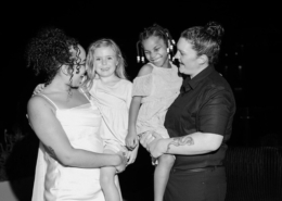 Black-and-white portrait of two brides smiling with two young girls in dresses during their Dreams Bahia Mita wedding celebration, capturing a sweet family moment together.